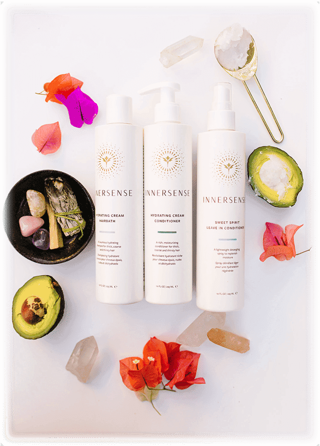 Innersense hair products with flowers, avocado, crystals, and incense in a flat lay arrangement.