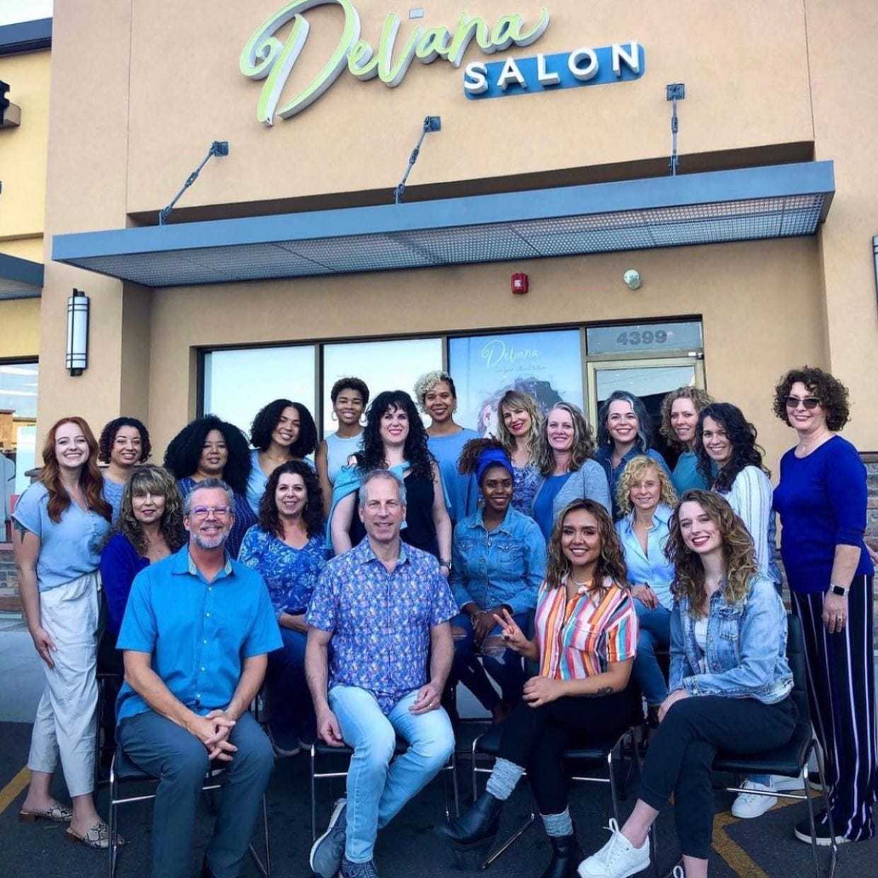Group of smiling people posing in front of Devana Salon entrance.