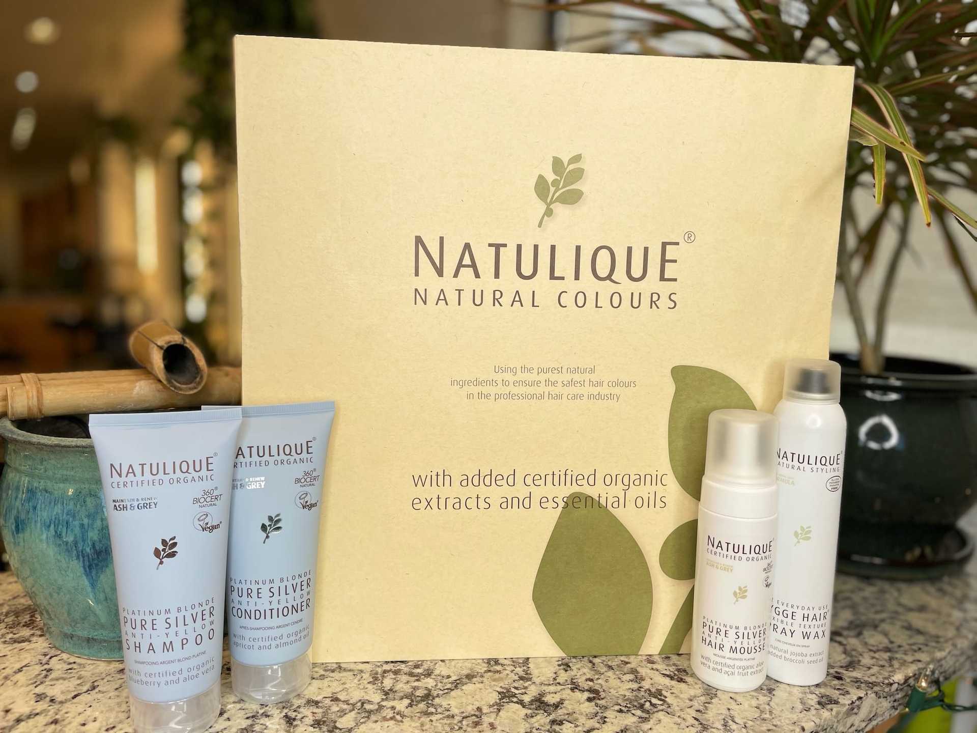 Natulique hair care products displayed on a table with a backdrop showcasing their natural benefits.